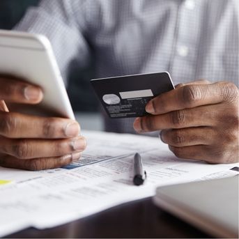 Person holding phone and credit card over documents